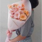 A bouquet of pink and orange gerbera daisies wrapped in light pink paper, held by a person in a grey shirt.
