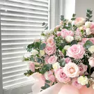 A bouquet of pink and white roses with greenery, against a white louvered background.