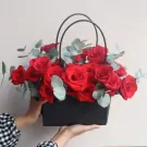 A black bag full of red roses and eucalyptus.
