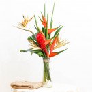 Tropical flower arrangement with red ginger, heliconia, and bird of paradise in a vase.