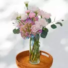 Pastel flower arrangement with roses, hydrangeas, and carnations in a glass vase.