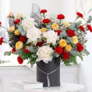 White peonies, red and orange roses in a black hat box with greenery and black ribbon.