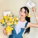 Woman in denim overalls holding a yellow rose bouquet and a Mother's Day card.