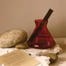 Minimal Mist Diffuser in a red glass bottle with a black reed diffuser stick and surrounding stones.