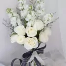White roses and stock flowers in a bridal bouquet with a dark blue and white ribbon.