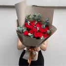 Bouquet of red roses with eucalyptus leaves, wrapped in brown paper and tied with a ribbon.