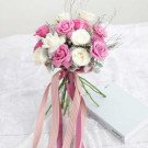 Bridal bouquet of pink and white roses with ribbon streamers on a lace cloth next to a light blue book.