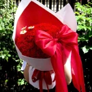 Bouquet of red carnations and wooden daisies with a large red bow.
