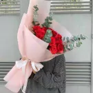 A bouquet of red roses with eucalyptus leaves, wrapped in pink paper and tied with a white ribbon.