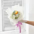 Rainbow rose bouquet with baby's breath, wrapped in white paper and tied with a purple ribbon.