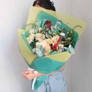 Woman holding a pastel bouquet wrapped in green and yellow paper.