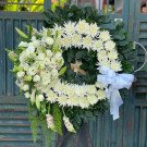 Funeral wreath with white roses, chrysanthemums, lilies, and greenery, adorned with a white ribbon.