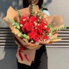 A bouquet of red roses and daisies wrapped in brown paper, held by a person.