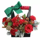Black basket with red roses, carnations, berries, pinecones, and a green bow.