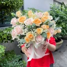 Pink and peach roses with baby's breath in a pink box, held by a person in a red shirt.