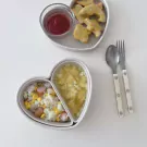 Heart-shaped lunchbox with rice, corn, sausage, soup, chicken nuggets, and ketchup.