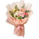 A bouquet of pink, yellow, and white flowers wrapped in peach and pink paper, tied with a pink ribbon.