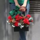Black flower basket with red roses and carnations, tied with a green bow.