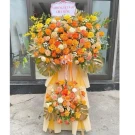 Grand flower stand for grand opening with orange and yellow roses, lilies, and monstera leaves.