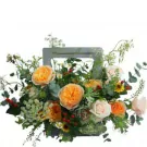 A floral arrangement in a wooden crate with orange and cream roses, daisies, and greenery.