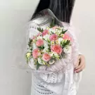 Bouquet of pink roses, white lisianthus, and small white daisies wrapped in sheer pink organza.