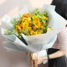 Yellow and orange flowers in a large bouquet wrapped in light blue paper, held by a person.