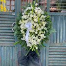 White funeral wreath with lilies, chrysanthemums, roses, and astilbe on a wooden gate.