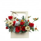 A floral arrangement in a light beige box with red roses, gold gerbera daisies, and eucalyptus leaves.