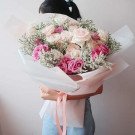 Bouquet of pink and white roses with baby's breath, wrapped in white paper and tied with a pink ribbon.