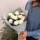 Bouquet of white roses with light blue and grey wrapping paper, held by a person in a blue shirt.