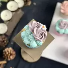 Mint and purple frosted cupcake with flower and gold leaf on a stand.