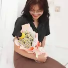 Woman in black shirt smiling and holding a bouquet of white and yellow flowers wrapped in pink and white paper.