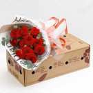 Bouquet of red roses in wrapping paper next to a cardboard box with floral designs.