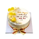 A white cake with yellow and white frosting flowers and hearts, and a yellow and brown ribbon bow.