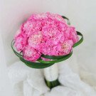 Pink carnation bridal bouquet with green leaves and white ribbon handle.