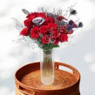 A vase of red and silver roses with dried flowers on a rattan tray.