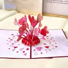 A 3D pop-up card with a bouquet of red and pink hearts exploding from the center.