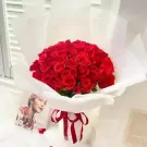 A large bouquet of 66 red roses wrapped in white paper, tied with a red ribbon.