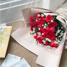Red roses and white daisies in a bouquet wrapped in cream paper.