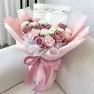 A bouquet of pink and white roses and other flowers, wrapped in pink and white paper with a pink ribbon.