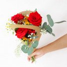 Hand holding a bouquet of red roses, sunflowers, and greenery in kraft paper.