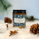 Amber candle with "Wood & Sea Salt" label and festive design, surrounded by pinecones and cotton on a white fuzzy surface.