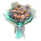 Pink roses with yellow accents in a turquoise bouquet, tied with a gray ribbon.