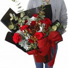 Red roses, carnations, pinecones, and eucalyptus in a bouquet with a red bow.