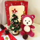 A teddy bear and a miniature Christmas tree sit on a table.