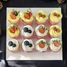 Assortment of 12 cupcakes with yellow and white frosting, topped with strawberries and blueberries.