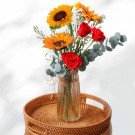 Bouquet of sunflowers, red roses, and eucalyptus in a vase on a rattan tray.