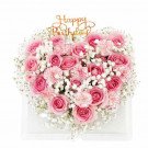 Heart-shaped floral cake with pink roses, carnations, baby's breath, and "Happy Birthday" topper.