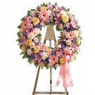 Funeral wreath with pink and yellow roses, lilies, and carnations on an easel.