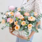 Basket of pink peonies, orange David Austin roses, and blue flowers with eucalyptus.